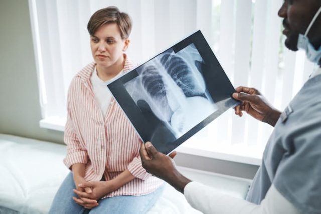 läkare som håller i en röntgenbild på lungor framför patienten som sitter oroligt på en bänk